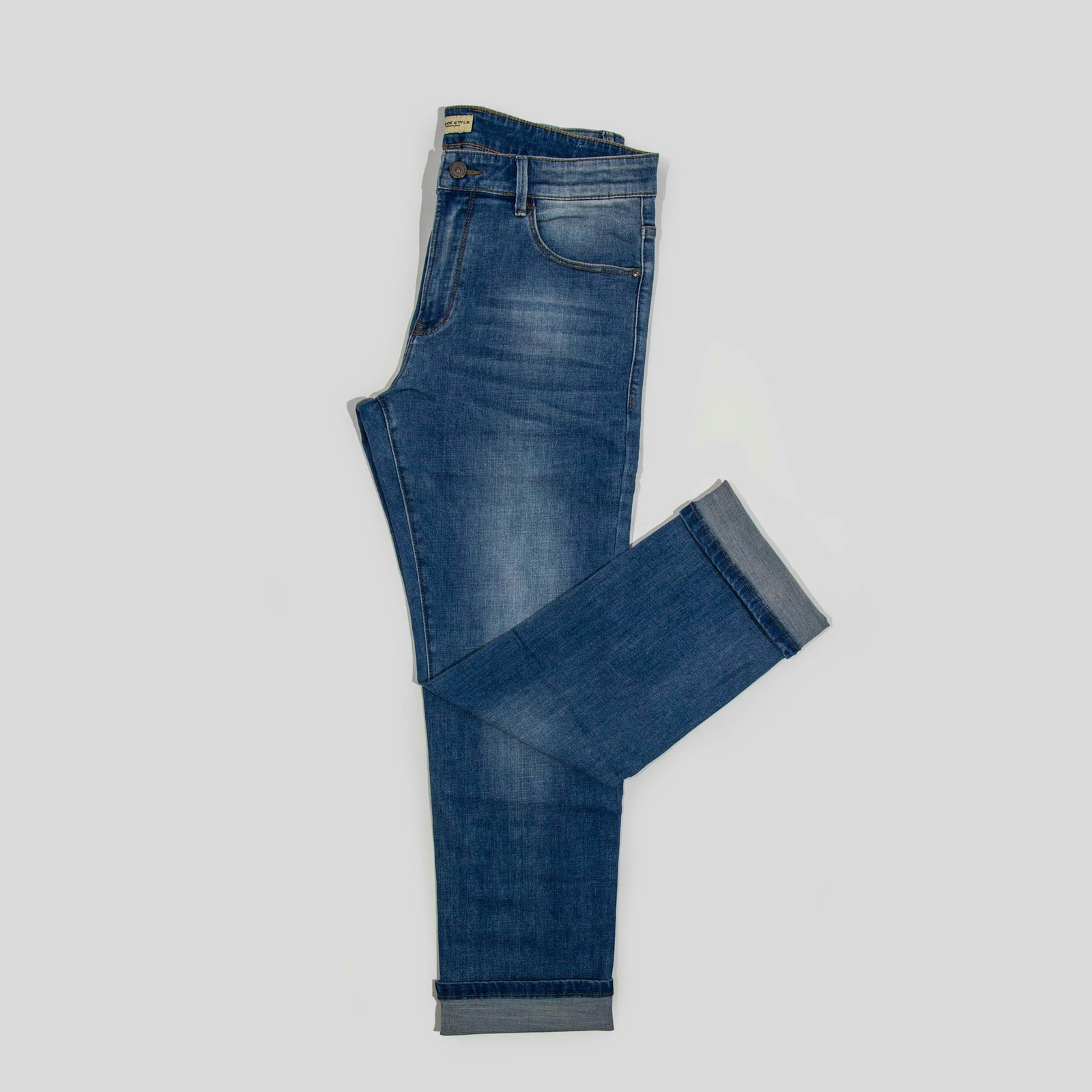 Dark slim jeans laid flat on a light grey surface, one leg folded across