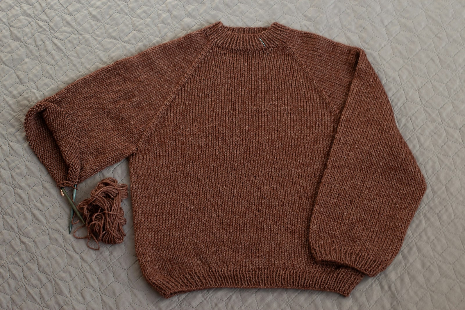 Rust hand-knit sweater laid flat on a grey knitted throw