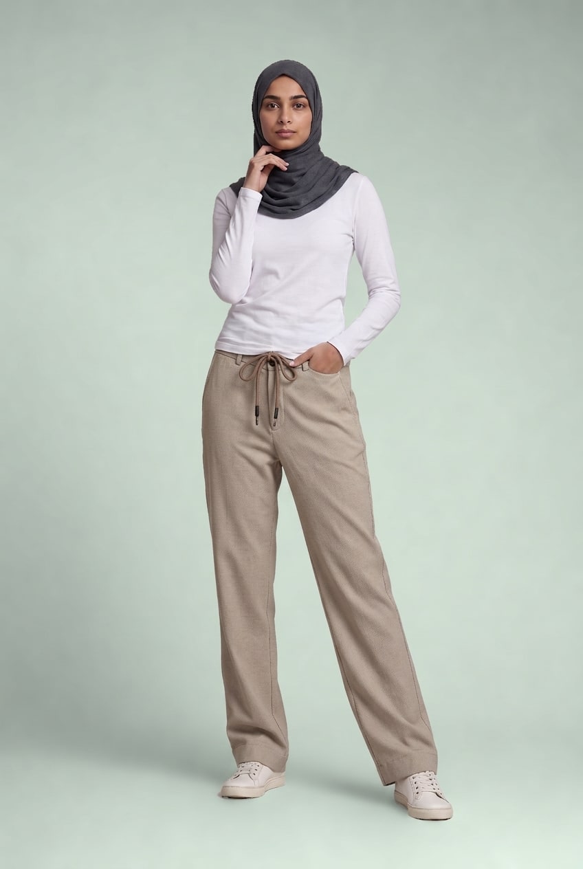 Model standing against a pale sage backdrop wearing the stone drawstring trousers