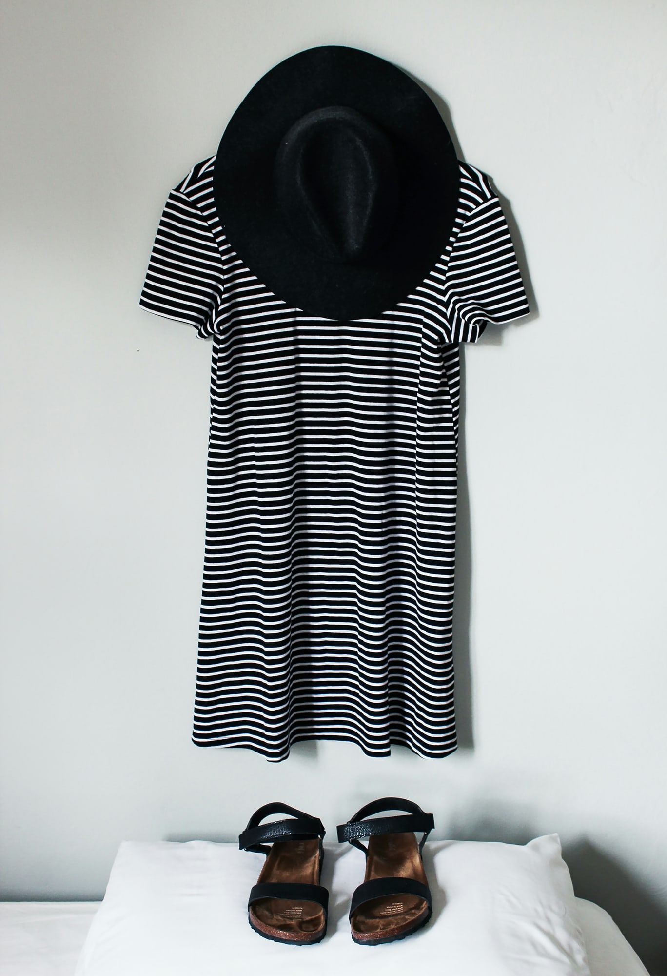 Striped t-shirt dress on a hanger against a white wall, with a black hat and sandals