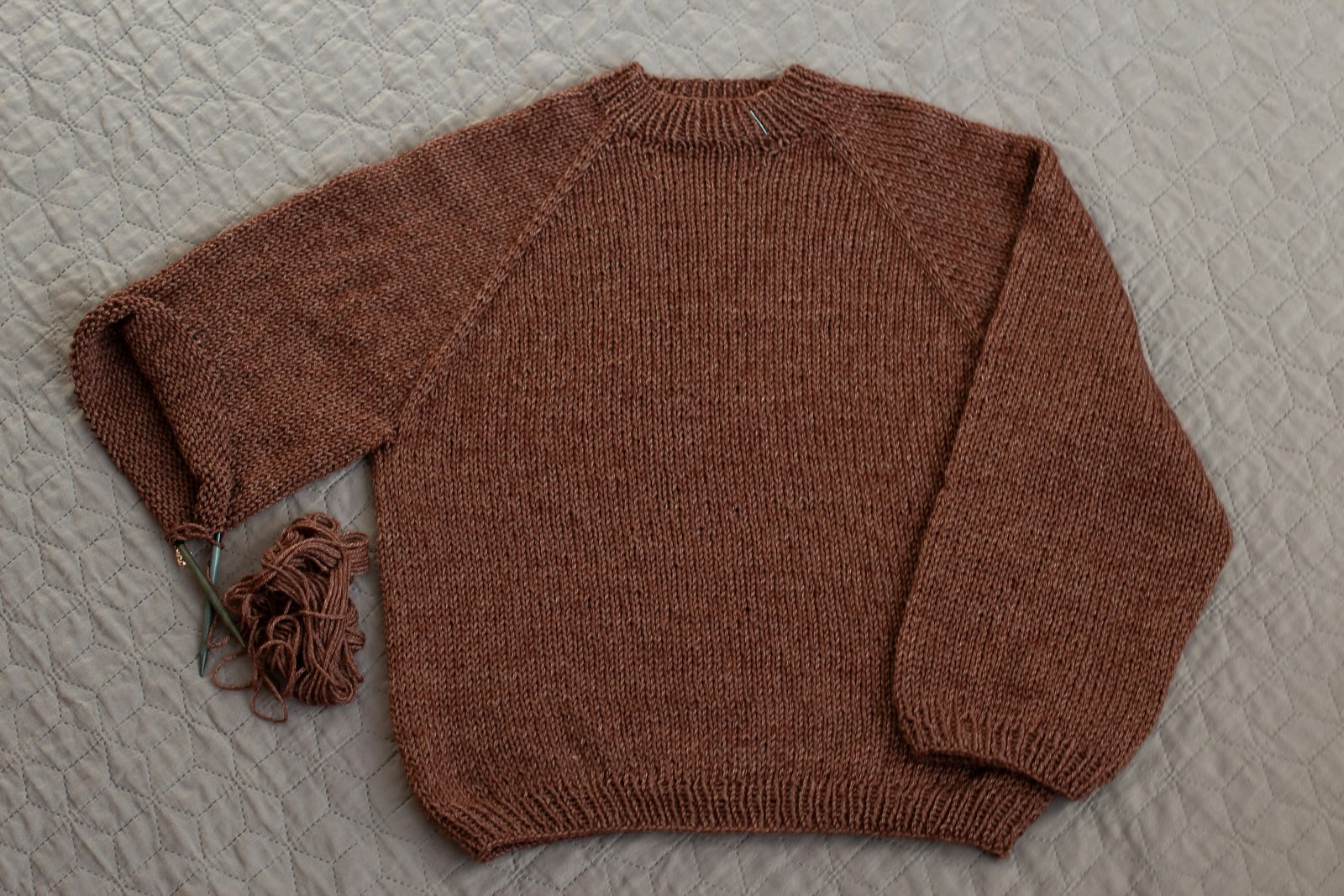 Flat-lay of a rust hand-knit sweater on a grey knitted throw