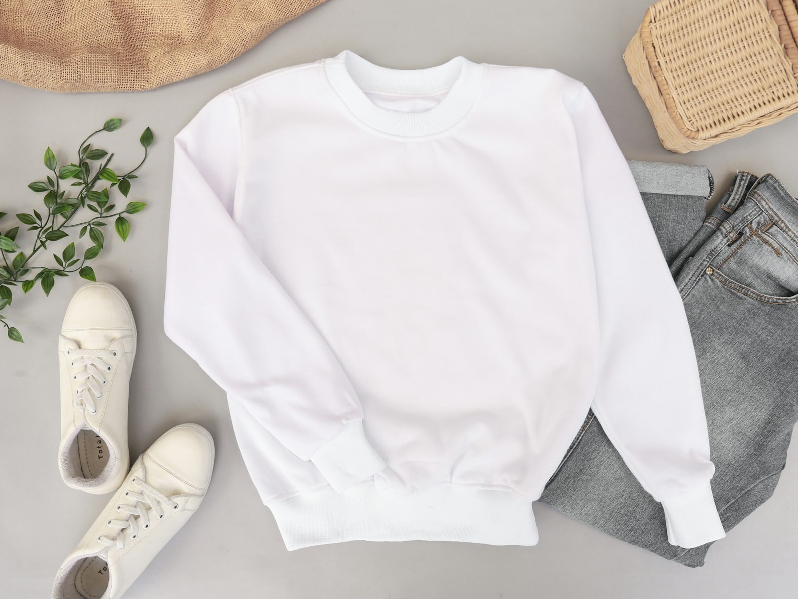 Flat-lay of a white crewneck sweatshirt beside grey jeans and white sneakers