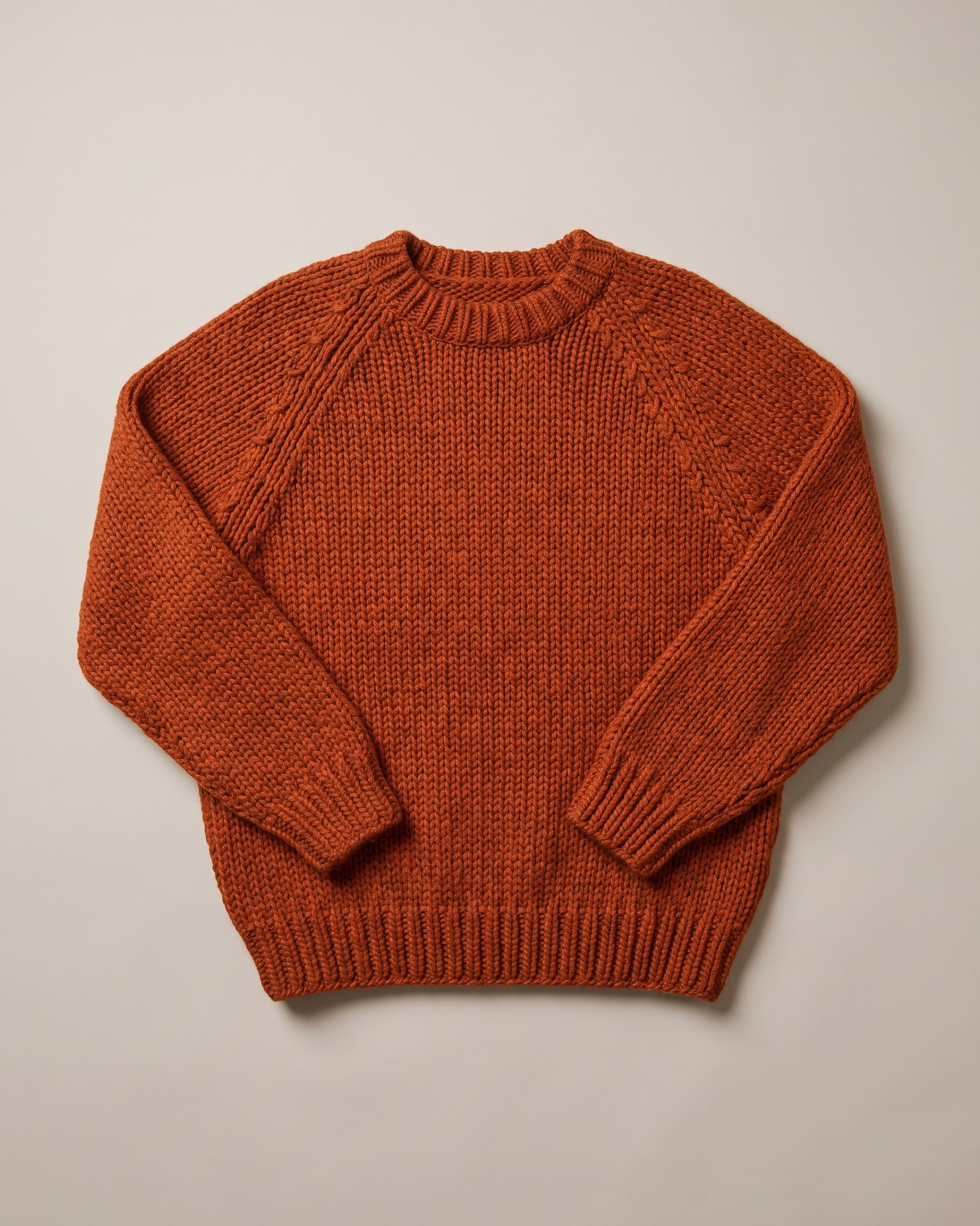 Flat-lay of a rust hand-knit sweater on light grey