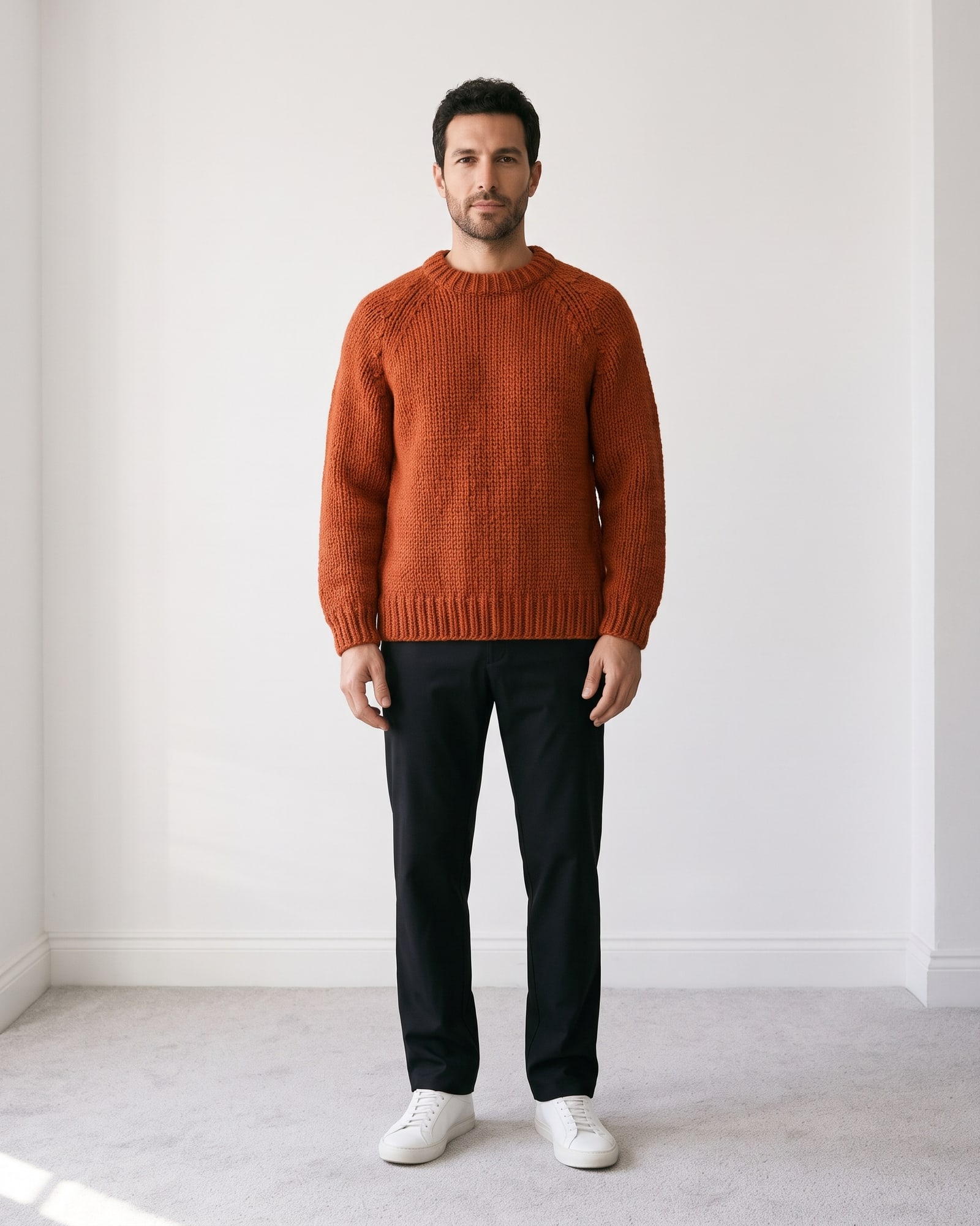 Male model wearing the rust hand-knit sweater in a grey room