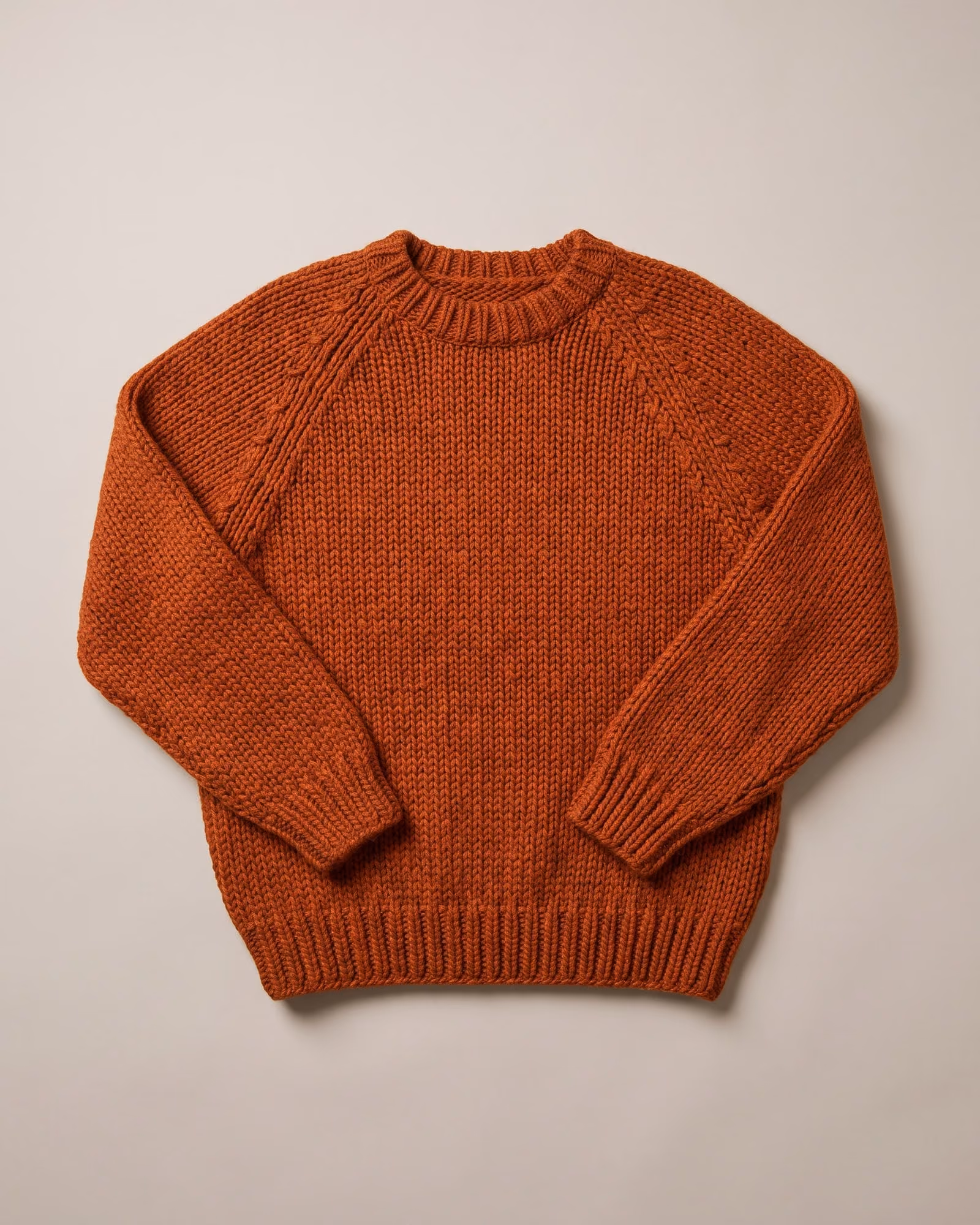 Flat-lay of a rust hand-knit sweater on light grey