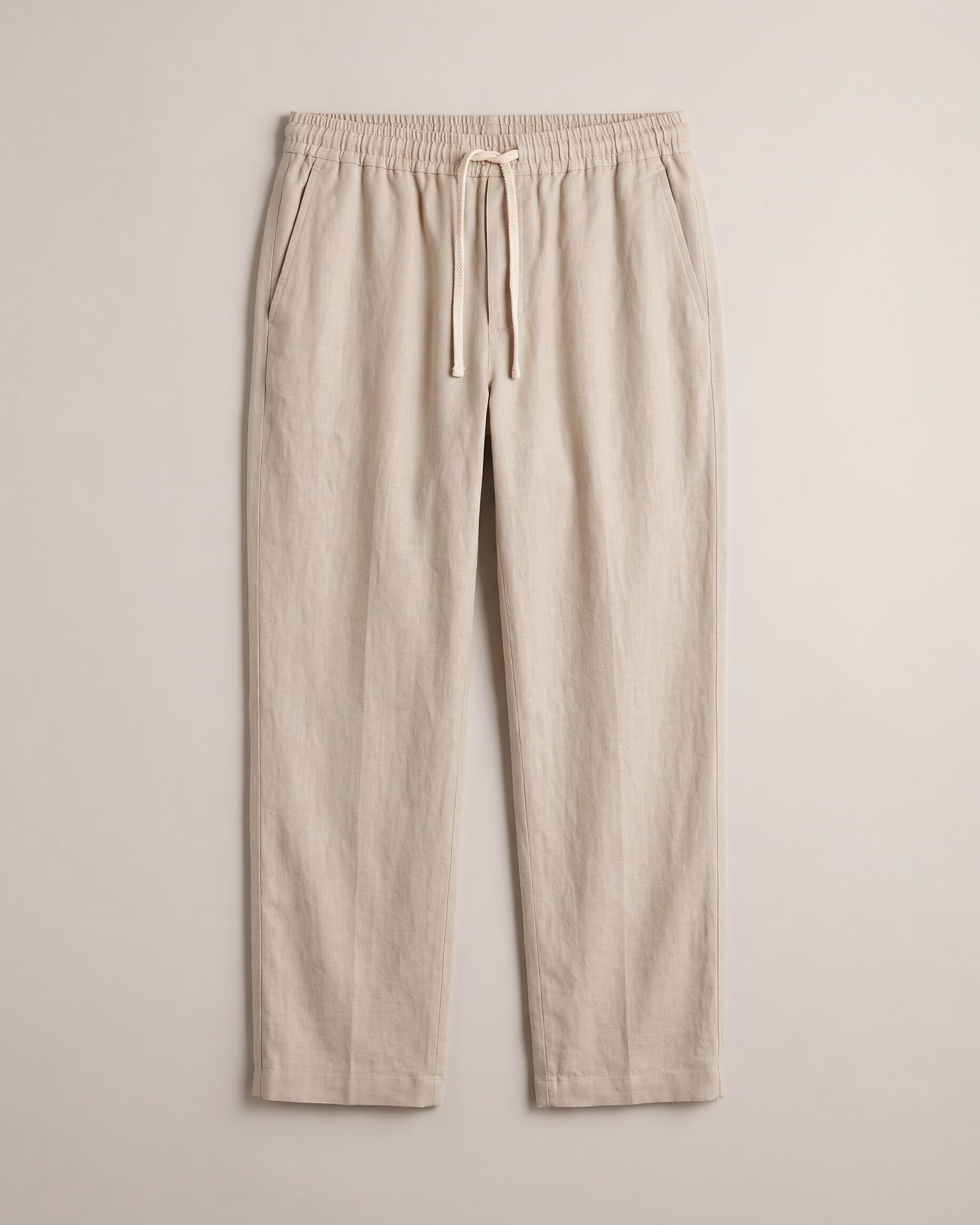 Flat-lay of stone drawstring trousers on light grey